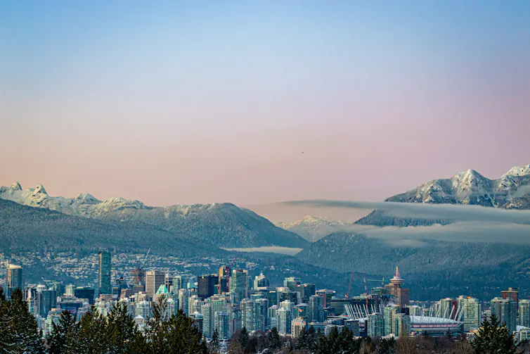 A city with skyscrappers, tall snowcapped mountains in the background