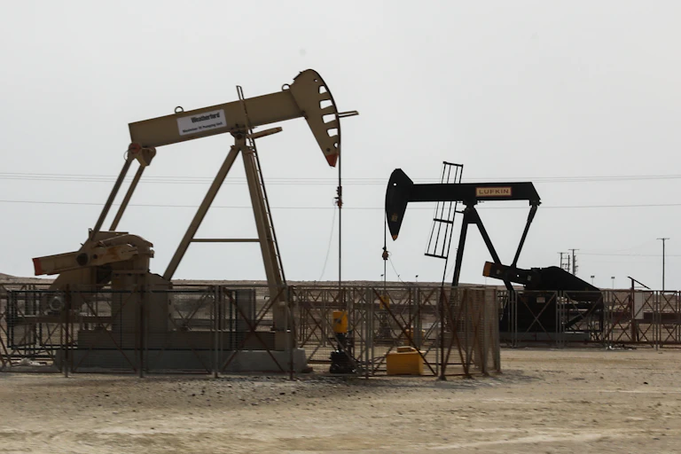 Two oil derricks sit on sandy ground.