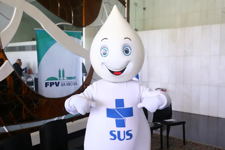A white vaccine droplet with a smiling face and the logo of Brazil's public health system on its belly.