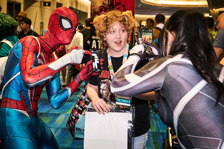 Una persona disfrazada de Spider-Man se besa con otra mientras alguien toma una foto con su teléfono.