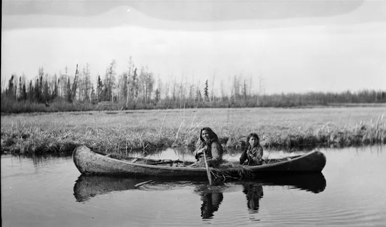 A black-and-white photo shows two men in a canoe.
