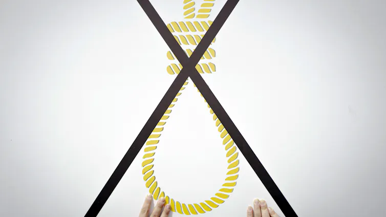 A person holds a large placard of a noose with a big cross through it.