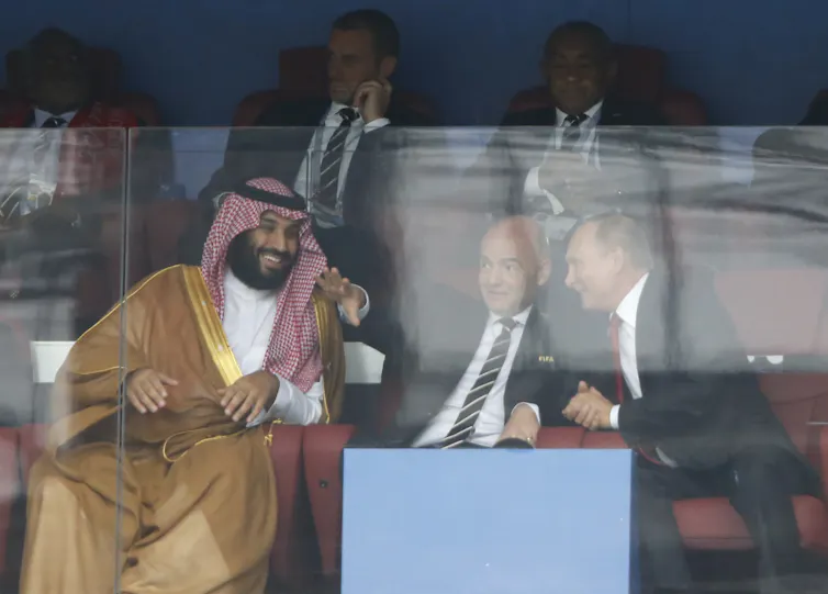 Canadá prohibirá los anuncios de combustibles fósiles antes del Mundial de 2026 1 Un hombre vestido de árabe con una capa marrón claro y un tocado rojo y blanco está sentado hablando con dos hombres vestidos con trajes oscuros.