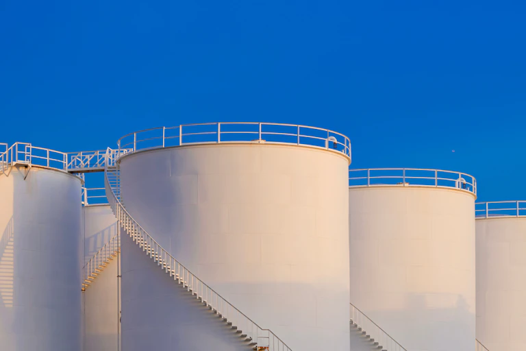 large white oil supply tanks against a blue sky.