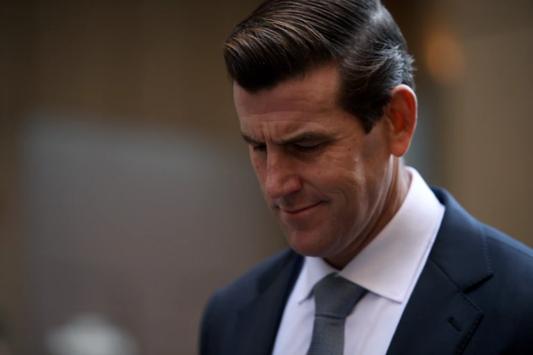 A close-up of a man wearing a suit, looking down and frowning