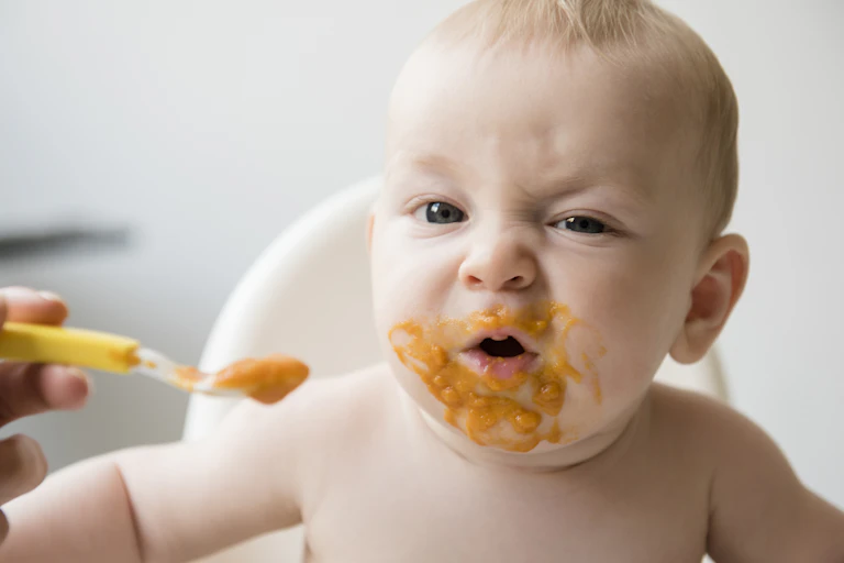 Baby eats orange-coloured puree while sitting in a high chair.