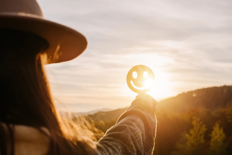 Side view of a person holding happy smiley face against a sunset