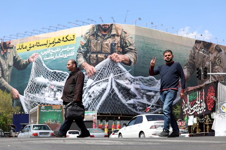 Iranians walk past a giant billboard proclaiming in Farsi script: 'The Strait of Hormuz will remain closed'.