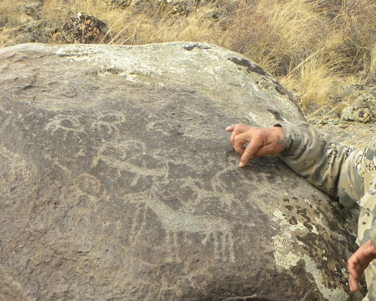 la mano de un hombre señala siluetas de animales sobre una gran roca