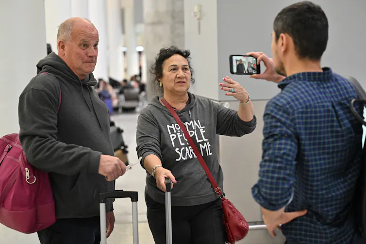 Un anciano y una mujer con equipaje hablan con un periodista.