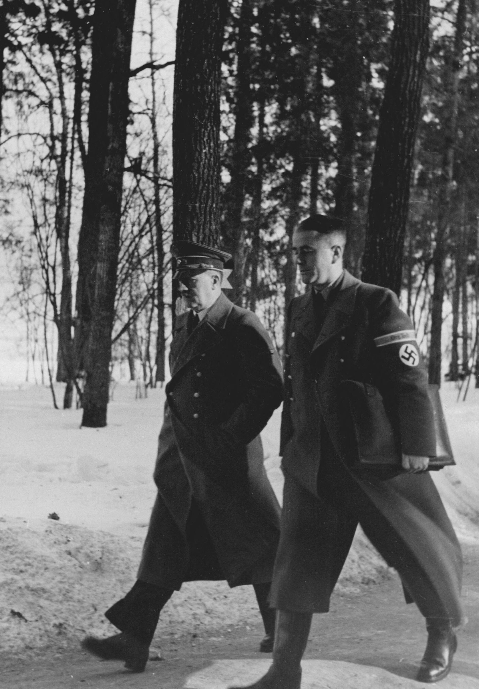 Speer walking next to Hitler in the snow. He wears a Nazi uniform.