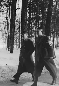 Speer walking next to Hitler in the snow. He wears a Nazi uniform.