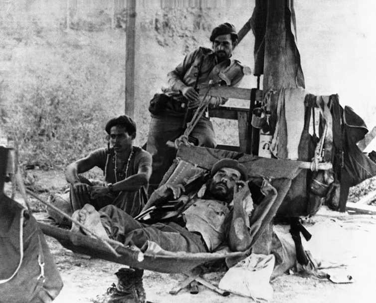 A black-and-white photo shows Cuban soldiers sitting in the shade.