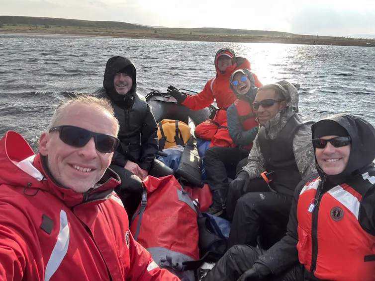 The team wearing red jackets in a zodiac boat on the ocean.