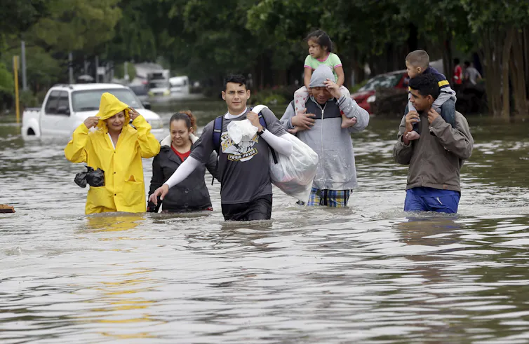 People carry their belongings in trashbags and adults have small children on their shoulders as they walk through waist-deep water.
