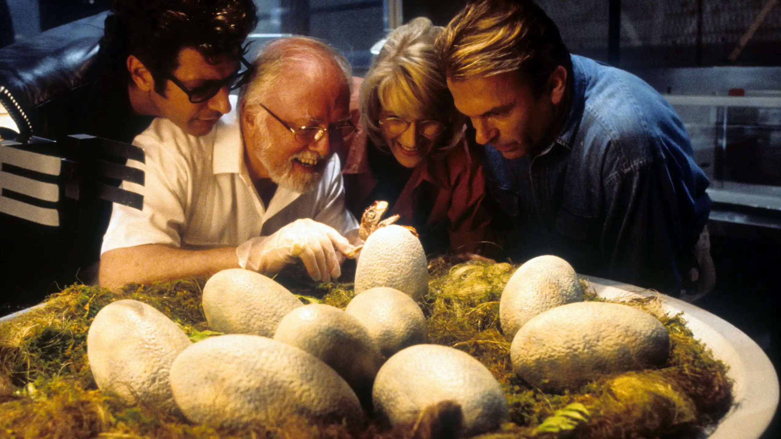 Imagem do filme “Jurassic Park” mostrando quatro pessoas examinando um ninho de ovos grandes e de aparência coriácea.
