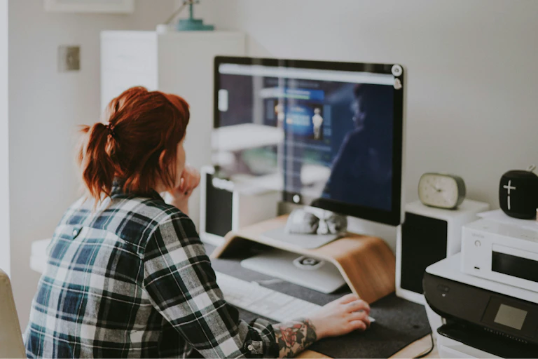 A woman sits at a desk in her home and works on a computer