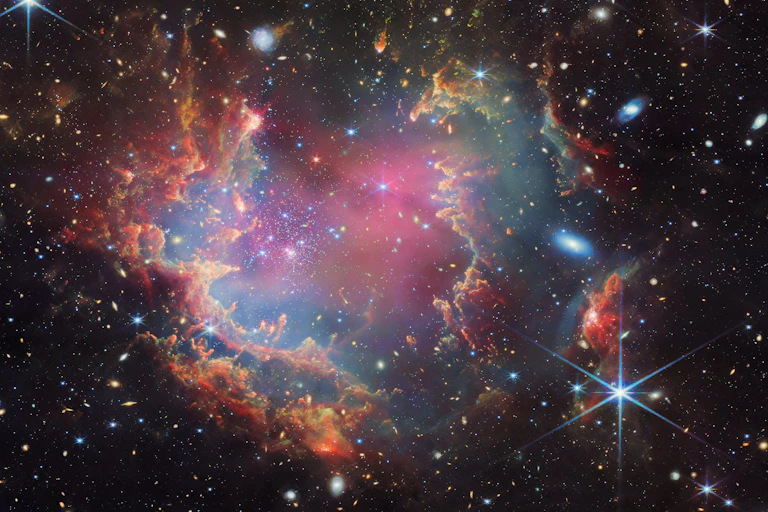 A star cluster is shown inside a large nebula of many-coloured gas and dust.