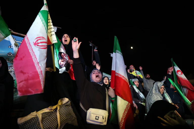 A crowd of people chanting and waving Iranian flags