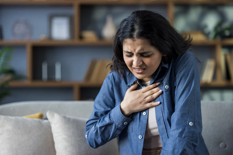A young woman holds her chest in pain.