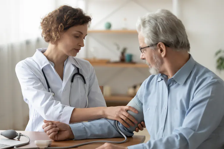 An older man has his blood pressure checked by a young female doctor.