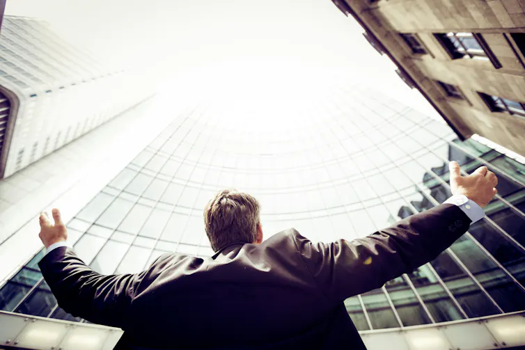 A man surrounded by buildings raises his arms to the sky