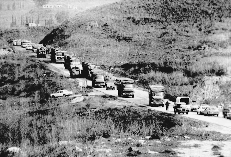 A convoy of military vehicles on a road in a date black and white photo.