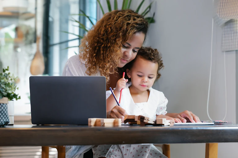 young smiling mother at a table with her child with her laptop open on the side.