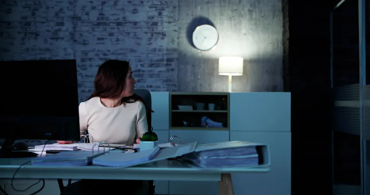 woman at work in a dark office looking at the clock on the wall.