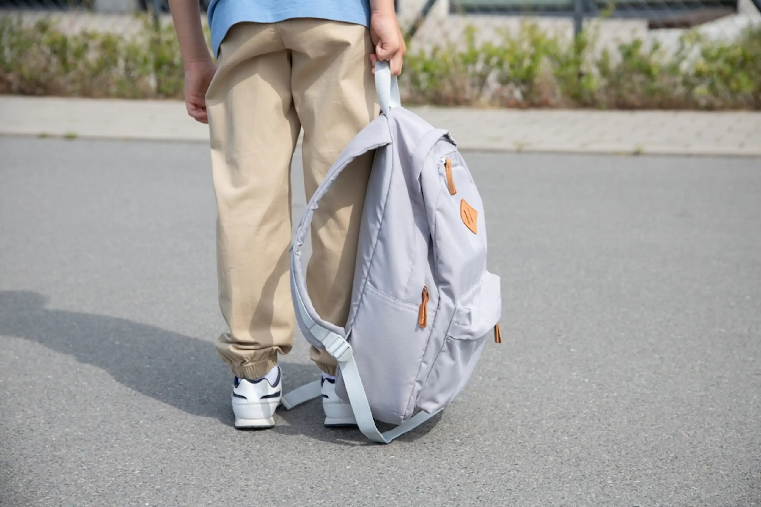 Un enfant qui tient un cartable à la main.