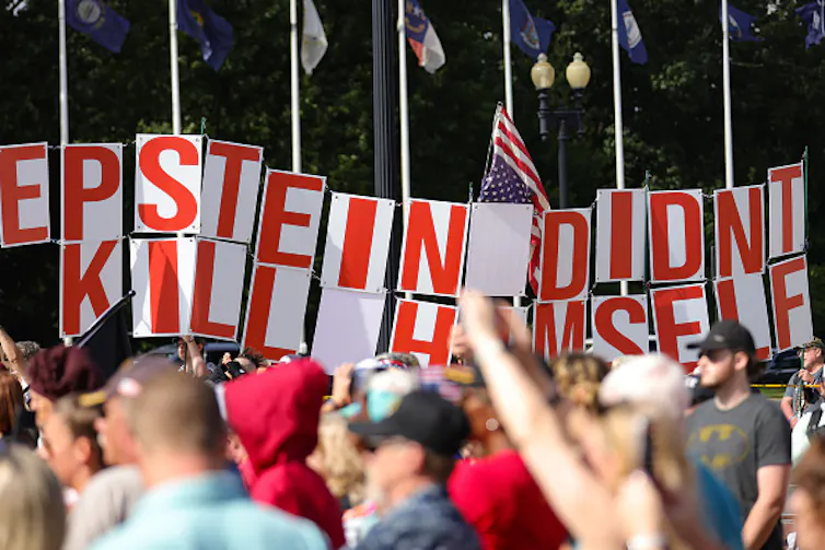 Protesters carrying signs about conspiracies.