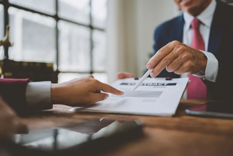 someone pointing to a section of a contract while another person offers them a pen.