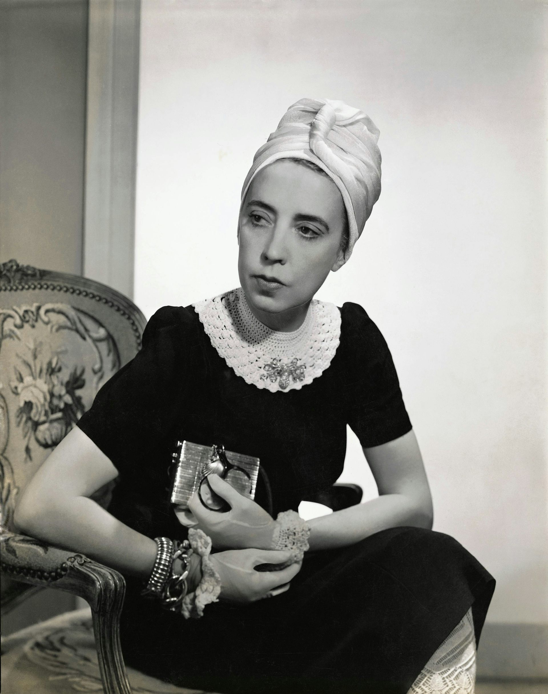 A stylish woman seated wearing a black crocheted dress and a turban.