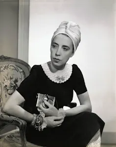 A stylish woman seated wearing a black crocheted dress and a turban.