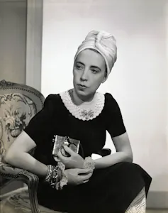 A stylish woman seated wearing a black crocheted dress and a turban.