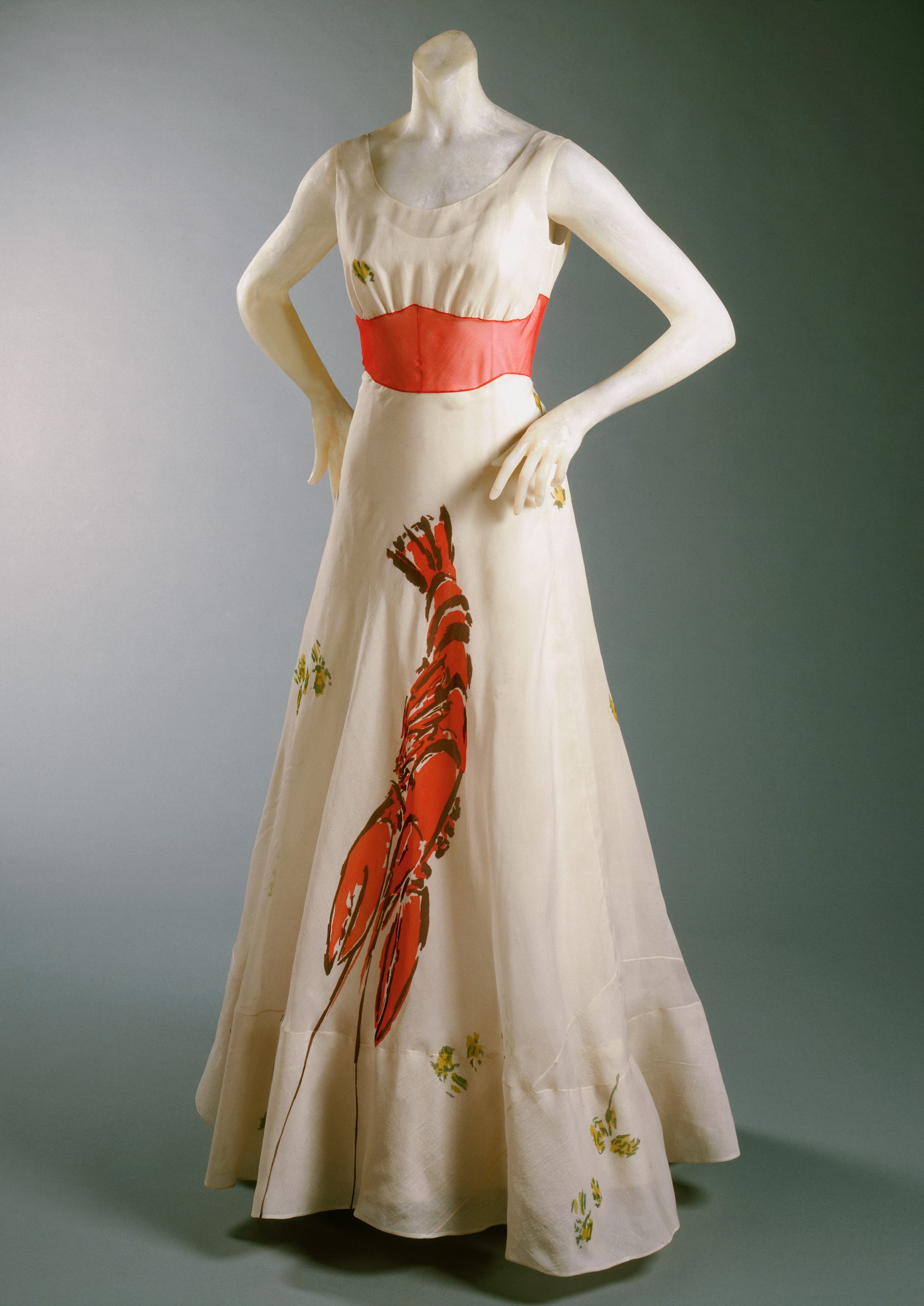 A mannequin in a cream sleeveless dress with coral waistband and a lobster stretching down the front.