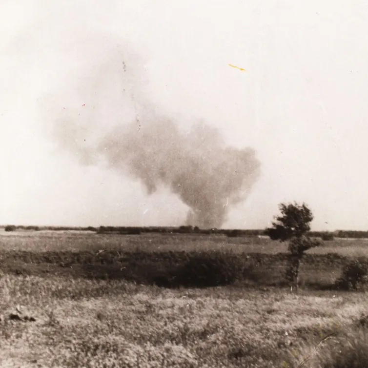 A black and white photograph shows a large smoke cloud rising over a field.