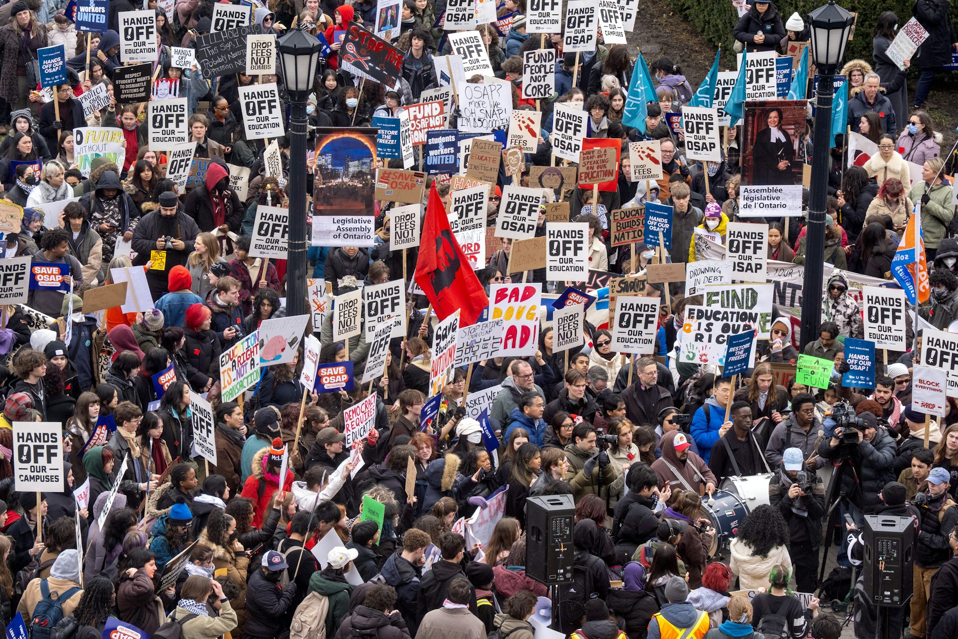 A large crowd of people with protest signs outdoors related to education cuts.