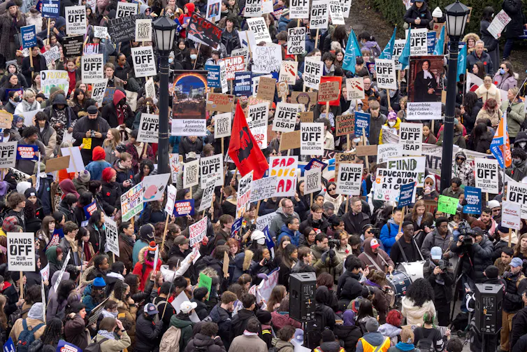 Gran multitud de personas con carteles de protesta al aire libre sobre los recortes en la educación.