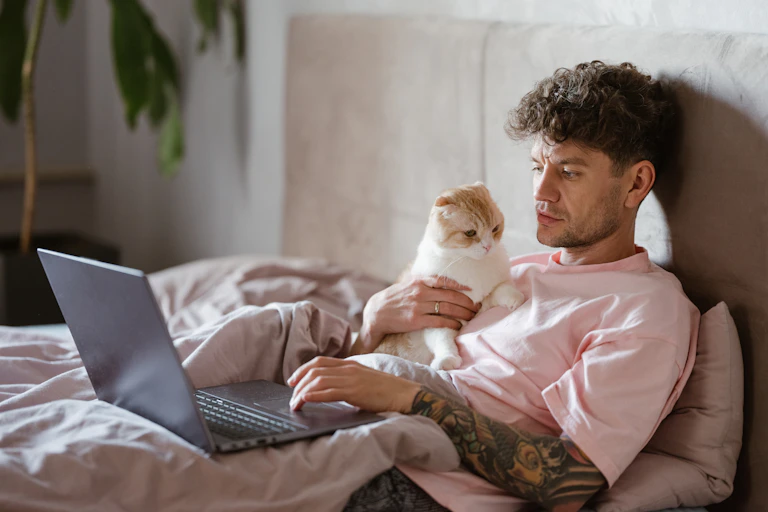 Man with sleeve tattoos does online therapy on his laptop while holding his cat