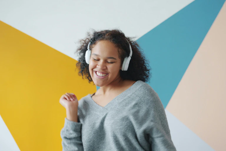 Young woman dances while listening to music, with a colourful wall behind her.