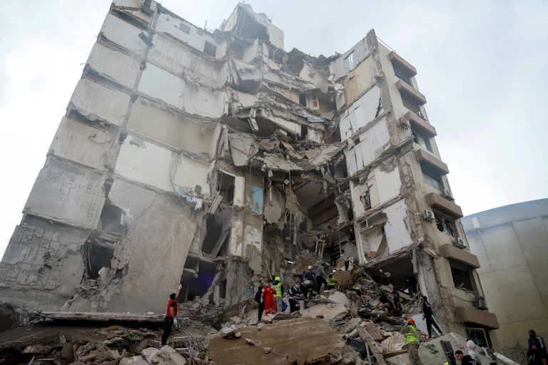 The wreckage of a multi-storey building with emergency workers at the bottom