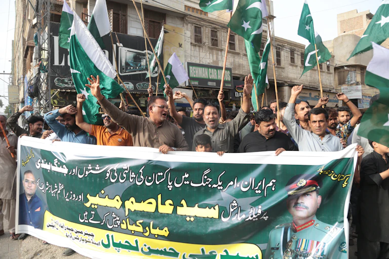 A crowd of people wave Pakistani flags at a rally while holding a large banner