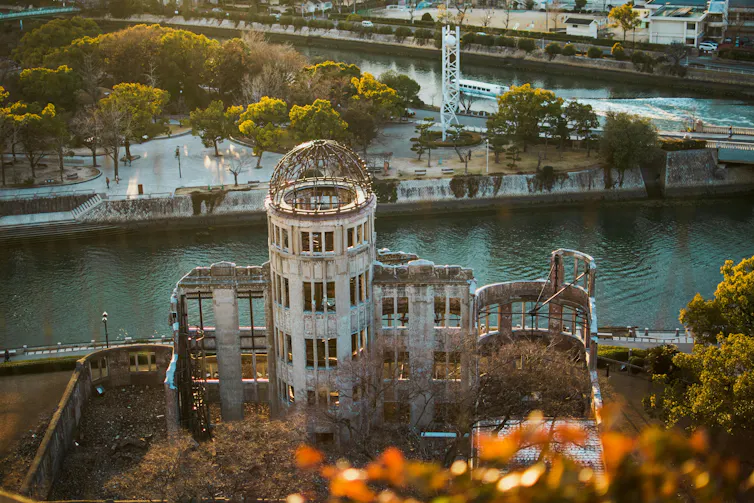 A skeletal old structure with an intact turret and facade against a river and a city in the distance.