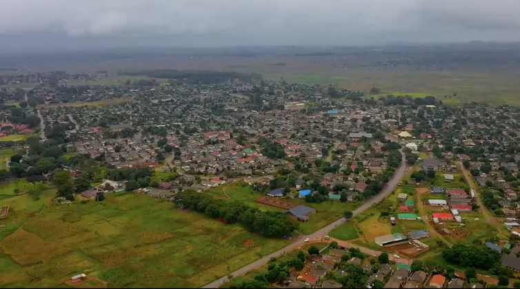An aerial view of a sprawling low-cost housing community in green fields.