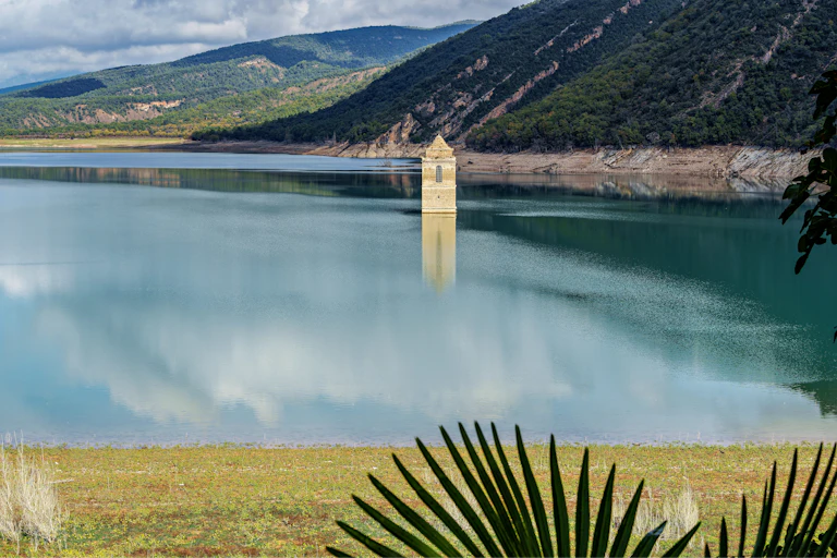 Un embalse rodeado de montañas del que emerge una iglesia