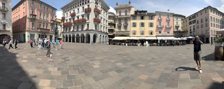 A wide angle of an open square with historic buildings, a man take a photo.