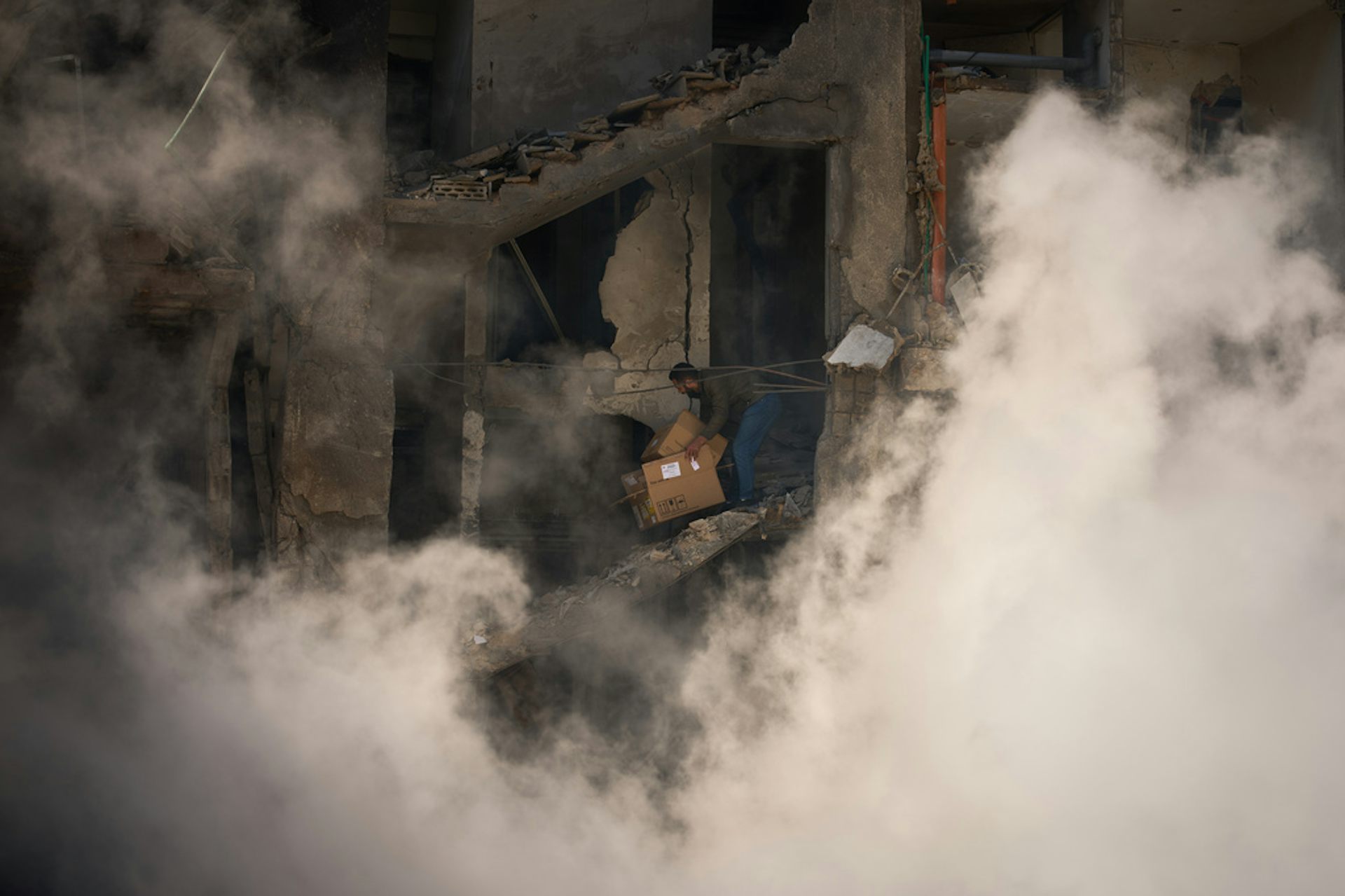 A man stands in a destroyed building as smoke rises around him.
