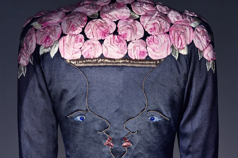 A dark blue jacket with embroidered faces in profile facing each other with pink roses on the shoulders.