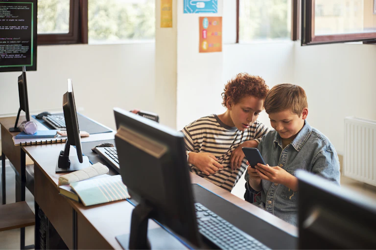 Dos niños mirando el móvil en un aula.